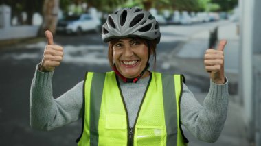 Bisiklet kaskı ve güvenlik yeleği giyen İspanyol kadın şehir sokaklarında coşkulu pozitiflik ve açık hava coşkusu sergiliyor..