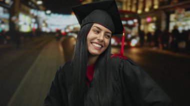 Mezuniyet üniformalı genç İspanyol kadın hareketli bir şehir caddesinde neşeli bir şekilde gülümsüyor..