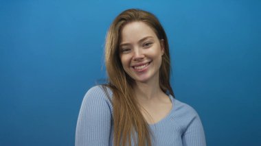 Mavi stüdyoda gülümseyen kadın yüzü tırtıklı kazak ve omuzlarından dökülen uzun saçlar; neşe.