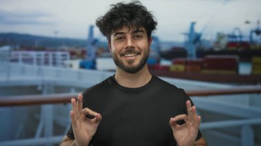 Genç İspanyol bir adam sakin bir şekilde meditasyon yapıyor. Gözleri kapalı, arka planda gemileri ve botları olan bir limanda. Denizcilik ortamında sükuneti somutlaştırıyor..