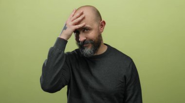 Sakallı ve dövmeli kel bir adam. Yüzü izole edilmiş sarı arka planda. Duygularını aktarıyor.