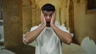 Beyaz gömlekli genç adam tarihi üniversite koridorunda duruyor ve duygularını aktarıyor..