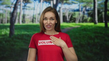 Kırmızı gönüllü gömlekli gülümseyen kadın sabah ormanlarında güneş ışığında ağaçların arasına elini koyuyor..