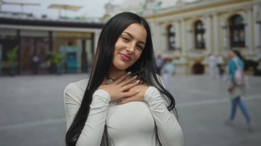 Açık havada gülümseyen, uzun siyah saçlı, şehir ortamında beyaz gömlek giyen, tarihi mimarinin bulanık arka planına sahip ve yürüyen insanlar..