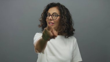 Gözlüklü ve beyaz tişörtlü İspanyol bir kadın, gri izole edilmiş arka plana güvenle işaret ediyor..