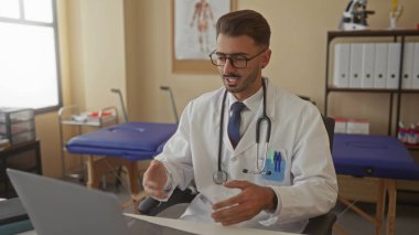 Steteskop ve dizüstü bilgisayarı olan genç İspanyol bir adam kalp şeklindeki jesti oluşturur; şefkat bakımı empati desteği.