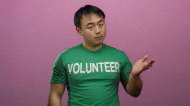 Yeşil gönüllü gömleği giyen genç adam, dışlanmış pembe arka plana karşı anlamlı bir pozda duruyor..
