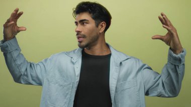 Açık yeşil bir stüdyoda el hareketleriyle konuşurken iki eliyle hareket eden bir adam..
