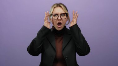 İzole edilmiş mor bir arka planda bağıran genç sarışın kadın, hayal kırıklığını açık ellerle ifade ediyor, gözlük takıyor ve duygusal bir jest olarak siyah bir ceket giyiyor..