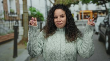 Kıvırcık saçlı, kazak giyen, şehir ortamında jest yapan bir kadın..