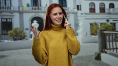 Binanın dışında telefonla konuşan, sarı kazak giyen, şehirde duygularını ifade eden, iletişim yaşam tarzını ve şehir deneyimini sembolize eden bir kadın.