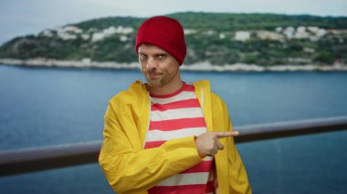 Sarı ceketli ve kırmızı şapkalı genç adam sahilde canlı ve neşeli kıyı titreşimleri sergiliyor..