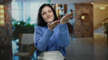 Zarif otel lobisinde elleri gösterişli bir kadın. Pozitif ve kendine güvenen bir duruş sergiliyor. Girişte parlak iç dekorasyonu olan mavi süveter giyiyor..