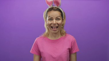 Genç sarışın kadın, kapalı gözlerle gülümserken tavşan kulaklığı ve pembe tişört giyerek stüdyoda elini kaldırıyor..