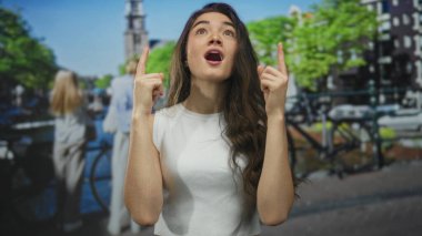 Görünür kaşları ve büzüşmüş dudakları ile geçen bisikletçiye kadınlar, işlek şehir caddesini işaret ediyor; onaylanmamış.