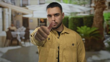 Güneşli restoran terasında, arkasında bulanık lokantalar ve yeşil bitkilerle baş aşağı hareket eden bir adam. Onaylamıyor..