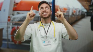 Elinde steteskop tutan sakallı genç adam açık deniz manzaralı yolcu güvertesinde duruyor..