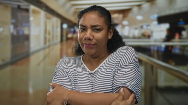 Çizgili gömlek giyen kadın dudaklarını bastırır ve parlak alışveriş merkezi cam koridorunda gözlerini kapatır; tefekkür.