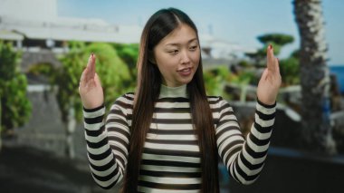 Genç Çinli kadın şehir sokaklarında hareketler yapıyor, açık bir gökyüzü altında neşeli ve çekici davranışlar sergiliyor..