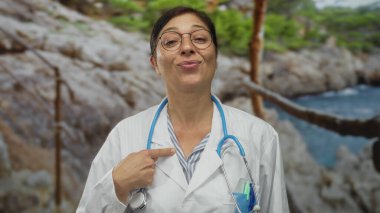 Beyaz önlüklü kadın doktor, güneşli sahil sahilinde steteskopla göğüs göğse işaret ediyor..