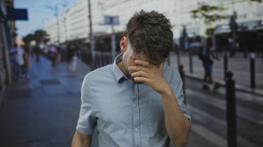 Kalabalık bir şehir sokağında gözlerini koruyan bir adam binalar ve otobüs durağı ile çevrili. Hayal kırıklığı..