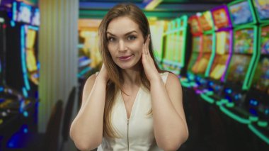 Genç bir kadın, kalabalık kumarhanedeki neon ışıklarının altında slot makinesinde iki eliyle kulaklarını kapatıyor; gürültü stresi.