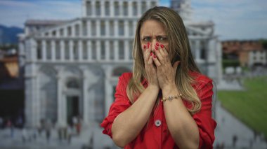 Kırmızı tişört giyen orta yaşlı bir kadın, tarihi binanın önünde elleri olan ağzı kapatıyor. Sürpriz..