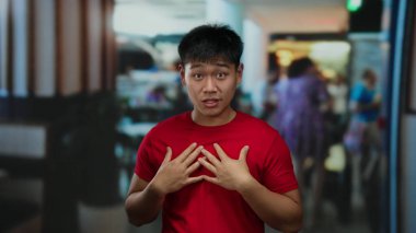 Kırmızı gömlekli genç adam hareketli bir otel ortamında coşkulu bir şekilde el kol hareketi yapıyor, sahneye enerji ve canlılık katıyor, hareketli ve çekici bir atmosfer yaratıyor..