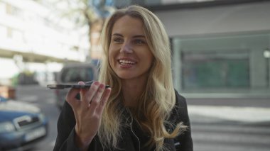 Şehir caddesinde akıllı telefondan konuşan bir kadın, güneşli gün ışığında gülümsüyor..