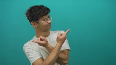 Gözlüklü beyaz gömlekli bir adam, tepe rengi stüdyo ortamında görülmemiş bir konuyu işaret ediyor..