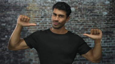 Siyah tişörtlü genç İspanyol bir adam stüdyoda duvara başparmak işareti yapıyor..