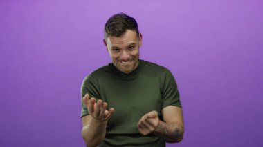 Genç adam mor bir duvara karşı jestler yapıyor, duygularını dışa vuruyor ve özgüvenli bir gülümseme ve günlük bir stil ile etkileşime giriyor..