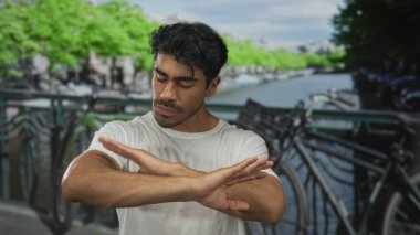Latin asıllı genç adam, bisiklet parkıyla sokak köprüsünde reddedilme jestini el sallıyor..