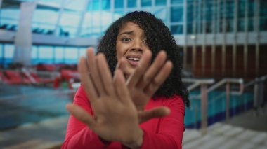 Kırmızı gömlekli kadın, korkmuş ifadesiyle avuç içlerini büyük cam bir binanın içine doğru itiyor; korku..