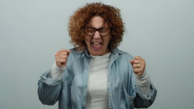 İzole edilmiş beyaz bir arka plan duvarının önünde duygularını ifade eden kadın, gözlüklü, orta yaşlı esmer bir kadını gösteriyor..