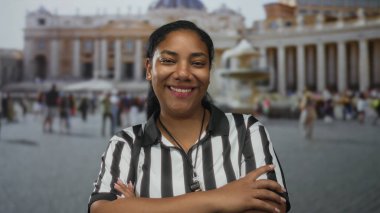 Kadın hakem, Vatikan meydanındaki tarihi bir kilise binasının önünde silah bağlarken gülümsüyor; güven.