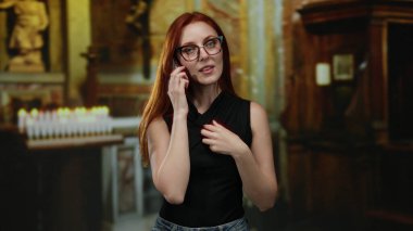 Genç, kızıl saçlı bir kadın kilise ortamında sessizliğe bürünüyor. Arka planda yanan mumlarla sağduyu ve sükunet taşıyor. Kapalı alan atmosferini yükseltiyor..