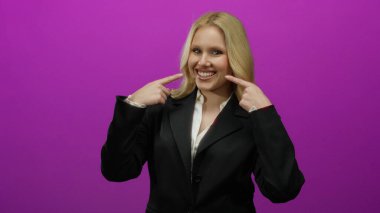 Kendine güvenerek gülümseyen bir kadın, parlak pembe bir arka plana karşı siyah bir takım elbise giymiş, pozitif ve profesyonellik saçan bir kadın..