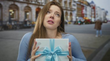Elinde mavi kurdeleli beyaz bir hediye kutusu olan kadın gündüz vakti şehir sokaklarında gözlerini kapatıyor..