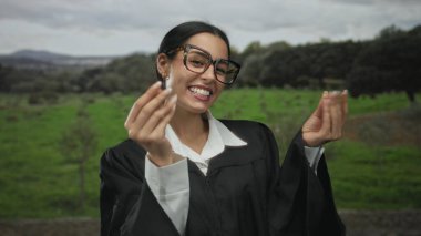 Hakim üniformalı İspanyol kadın parkta neşeli bir ifadeyle el kol hareketi yapıyor, yeşil doğayla iç içe yakalanmış, kıyafetine canlı bir kontrast sunuyor..