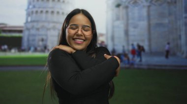 Pisa 'nın önünde kucaklaşırken kollarını kavuşturan kadın açık havada tarihi bir kulenin yanında Latin tarzı genç bir Latin göstermiş..