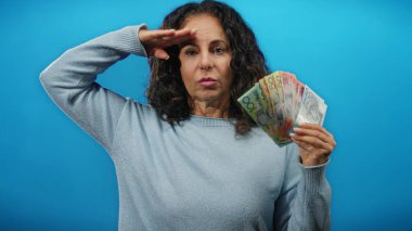 Avustralya doları tutan orta yaşlı bir kadın, mavi izole edilmiş bir arka plana selam veriyor, ışık ayarında para gösteriyor..