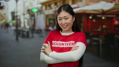 Şehir sokaklarında güvenle gülümseyen kırmızı gönüllü gömlekli, şehir arka planında bulanık bir kadın, modern Asyalı kimliğini ve açık havada toplum ruhunu yakalıyor..