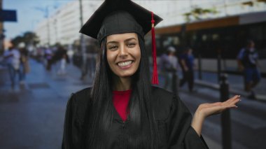 İspanyol kadın mezuniyeti başlık ve cübbe puanlarıyla kutluyor kalabalık bir şehir sokak arkaplanına karşı neşeyle, açık havada gençlik başarısının özünü yakalıyor..