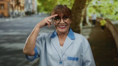 Üst düzey İspanyol kadın güler yüzlü bir şekilde şehir caddesinde dikilirken üniforma ve gözlük takar neşeli ve arkadaş canlısı tavırları sergilerdi..