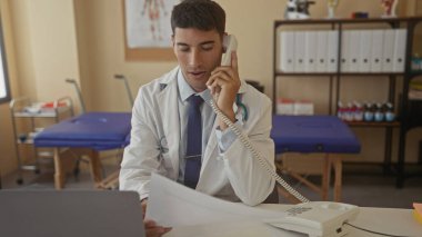 Adam telefonu kulağına tutuyor ve klinikte masa başında otururken kağıt okuyor; profesyonel danışmanlık.