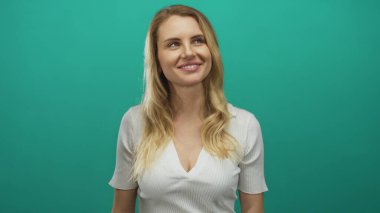 Beyaz gömlekli bir kadın canlı yeşil bir arka plana gülümsüyor, sarı saçlar omuzların üzerinden dökülüyor, sakin ve neşeli bir sahne yaratıyor ve kendine güveni ve güveni uyandırıyor..