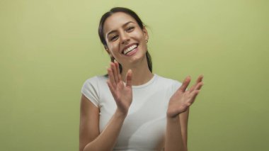 Genç İspanyol kadın, izole edilmiş sarı bir arka plana sevinçle el çırpıyor ve gülümsüyor. Mutluluk ve pozitiflik taşıyor..