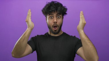 Sakallı genç İspanyol bir adam, parlak mor bir arka plana karşı elleriyle yüzünü örtüp açarken ciddi ve gülümseyen yüz ifadeleri arasında gidip geliyor..