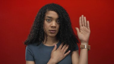 Ciddi ifadesi olan bir kadın elini göğsüne koydu ve diğer eli kırmızı stüdyo arkaplanına kaldırdı; samimiyet.